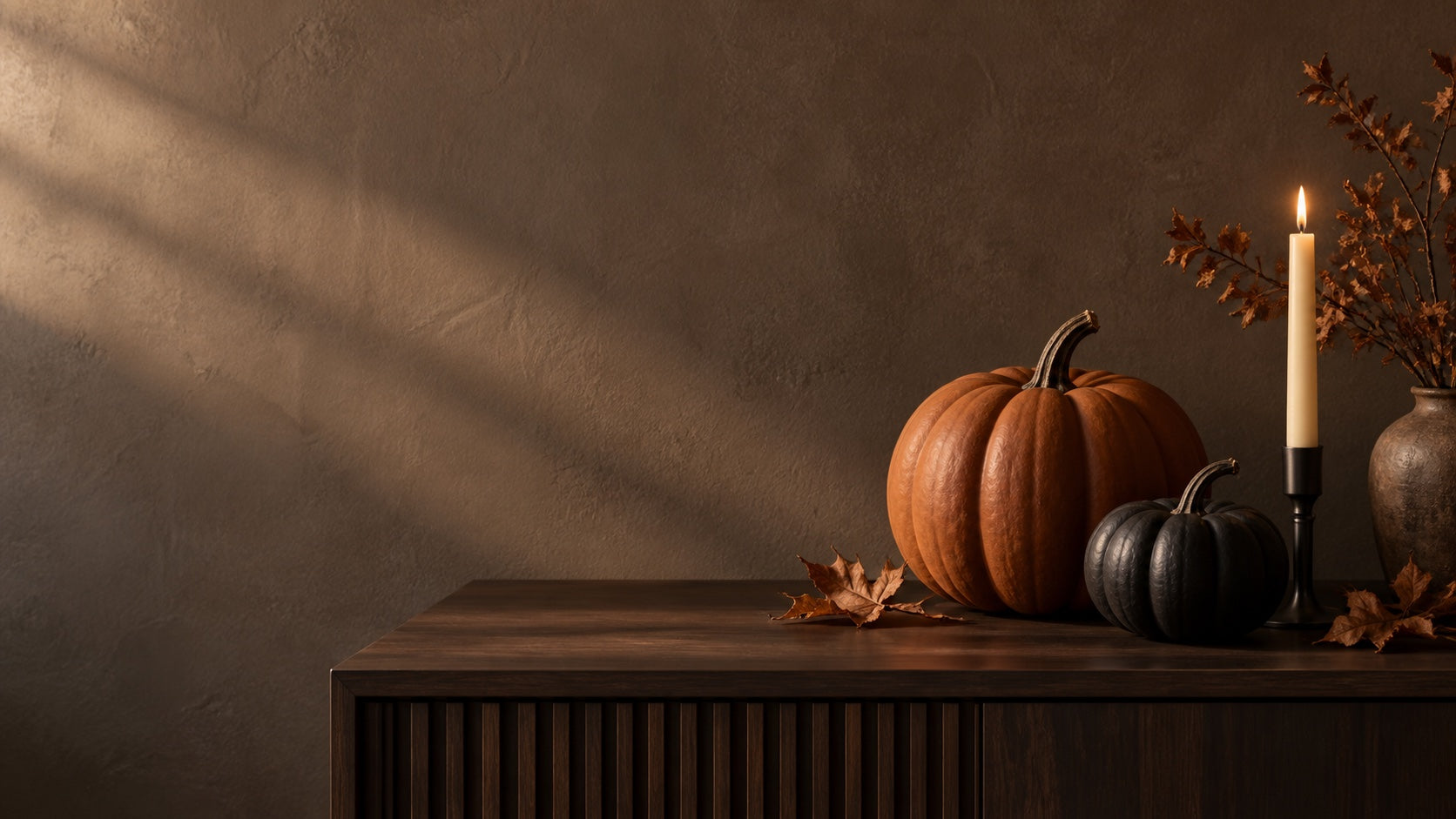 Orange and charcoal pumpkins with a candle on a dark walnut table.